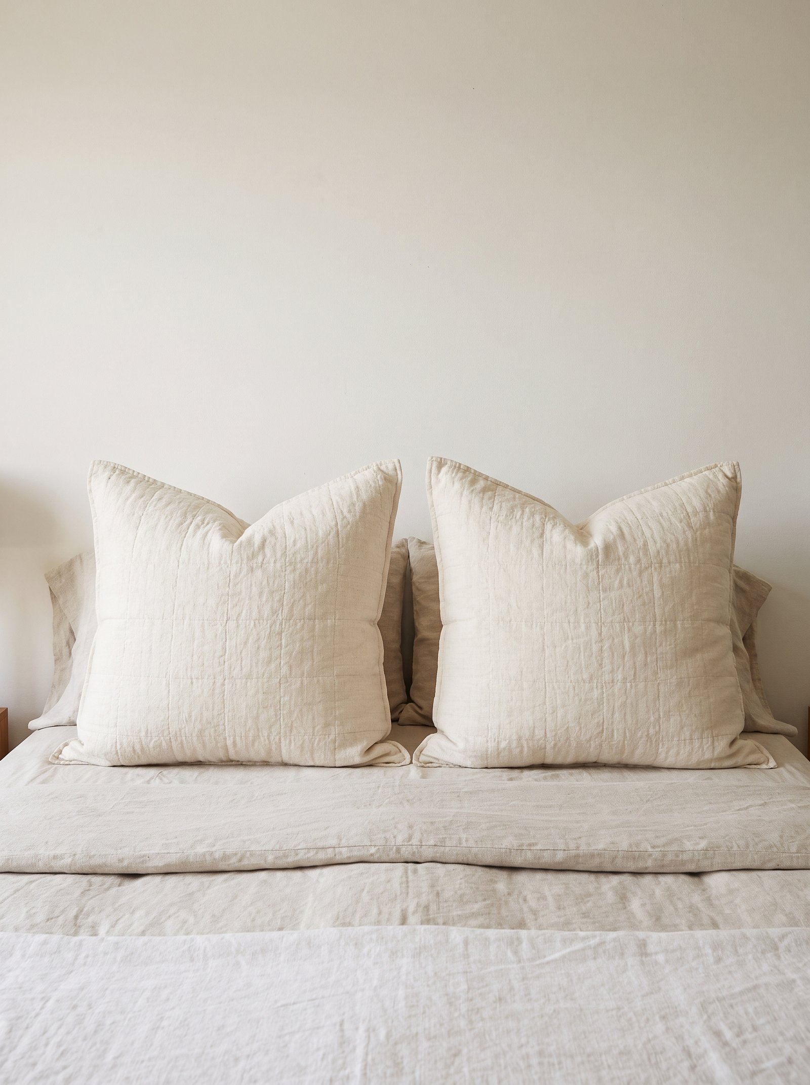 Upholstered bench at the foot of a styled bed holding a folded throw blanket and a book